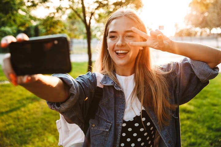 Eine junge Frau macht ein Selfie in einem Park bei Sonnenuntergang, während sie lächelnd posiert. Das Bild symbolisiert den Trend, Bewerbungsfotos mit KI zu erstellen, indem alltägliche Fotos digital optimiert werden